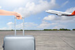A human hand holding a suitcase with an airplane flying on a blue sky background. Ready for traveling