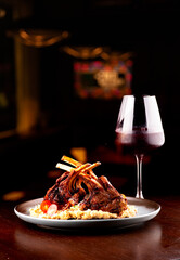 grilled rack of lamb with potato compote paired with glass of red wine on blurred bar background