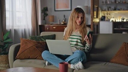 Wall Mural - Remote worker reading message at smartphone sitting home couch with laptop.