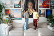 Creative married couple with high-five gesture finished decorating walls of home art studio hanging pictures while standing on couch together. Joyful man with woman designers delighted with result.