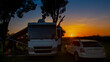 Rv motorhome and tow vehicle parked at campsite with sun in background