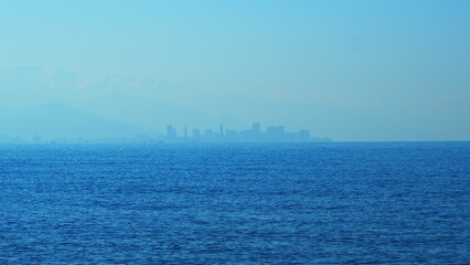 Skyscrapers On The Shore Of The Bay. Mountains Illuminated By The orange Rays Of The Rising Sun. Still.