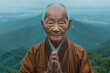 Old Buddhist Monk dressed in orange monk's robe, in his 80s, amiable, folding his hands upwards, standing on a mountaintop