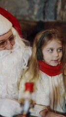 Wall Mural - Pretty little girl sitting with Santa Claus in front of the Globe model. Santa in red and white suit looking at globe together with a child at Christmas. Vertical video