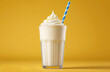 milkshake glass with topping and straw on solid yellow background.