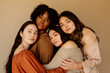 © Natalia - Women of different ethnicities and body types standing in front of a beige background hugging one another. Unity, participation, diversity, multicultural society. Women power.