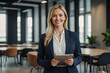 © eman - blond businesswoman wearing suit standing in office  smiling holding tablet, Confident Success in the Workplace