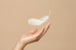 Female hand with feather on beige background, closeup. Space for text
