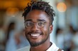 © Larisa AI - Close-up of a cheerful young African American man with glasses and curly hair looking at the camera, indoors with a blurred background