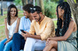 Group of young, multicultural friends - laughing and looking at a smartphone together in an urban park - social, leisure, connected.