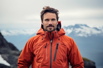 Wall Mural - Portrait of a merry man in his 30s wearing a functional windbreaker isolated on snowy mountain range