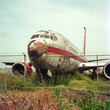Decommissioned airplane resting in overgrown field behind fence.