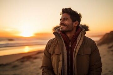 Sticker - Portrait of a blissful indian man in his 20s wearing a warm parka on beautiful beach sunset