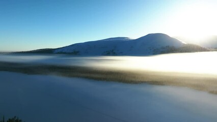 AERIAL: Icy mist cloud above a lake with sunrise and snowy mountain background