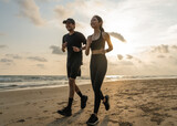 Fototapeta Sawanna - Asian Couple jogging and running outdoors sea sand beach. Sporty people wearing sportswear jogging. Male female athlete running during sunset on the beach. Workout exercise. Healthy and lifestyle.
