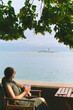 View with boat floating on lake Geneva, Switzerland, seen through summer restaurant or bar with woman relaxing on terrace with glass of vine, vacation in Europe