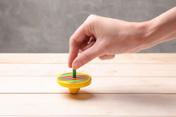 Wall Mural - Woman playing with bright spinning top at light wooden table, closeup