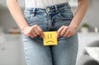 Cystitis. Woman holding sticky note with drawn sad face at home, closeup