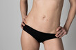 Belly of a very thin woman wearing black briefs. Detail of the belly, seen from the side.  The girl rests both hands on her hips.