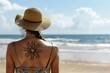 © Deivison - Woman with her back on the beach wearing a hat with a tattoo in the shape of a sun, concept of summer, leisure.