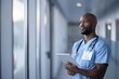 © senyumanmu - Thoughtful mid adult male nurse holding digital tablet while looking through window in corridor at hospital