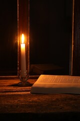 Wall Mural - Burning candle and Bible on wooden table near window at night