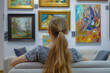 Rear view of young woman sitting on couch and looking at the painting