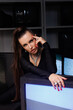 © Tatyana - A beautiful girl in a black jumpsuit with an open neckline and high heels, against the backdrop of old working TVs standing in a row. A portrait of girl with bright makeup, winged eyes, big lips.