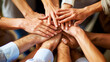 © thanakrit - A group of diverse people joining their hands together over a dark background.