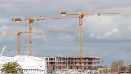 Wall Mural - Large construction site including several cranes working on a building complex, with cloudy sky timelapse. Riverside with walking bridge on a waterfront. Lisbon, Portugal