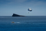 Fototapeta  - Parasailing - a parachute, a boat, an unforgettable experience and Isla de Benidorm in the background. Smile concept