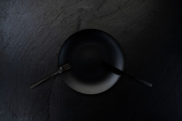 Black plate with fork and knife on dark table