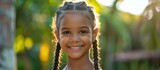 Fototapeta  - A young girl with braids in her hair smiling directly at the camera. She appears joyful and engaging.