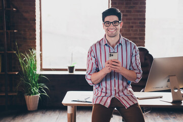 Poster - Portrait of young man office worker hold smart phone sit desk wear shirt loft interior business center indoors