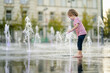 Cute little boy having fun with water in city fountain. Child playing water games outdoors on hot day. Summer activities for children.