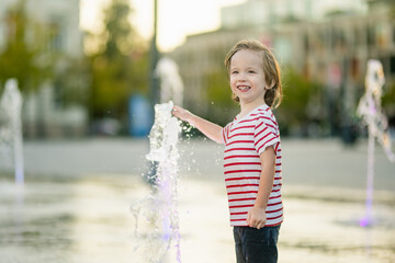 Wall Mural - Cute little boy having fun with water in city fountain. Child playing water games outdoors on hot day. Summer activities for children.