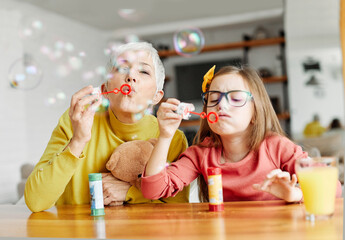 Wall Mural - child grandparent granddaughter grandmother bubble soap blowing fun together girl grandchild family senior smiling woman female happy adult lifestyle generation childhood togetherness