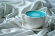 popular blue matcha tea in a white cup on silk white fabric. Blue algae spirulina, butterfly pea flower or blue matcha powder