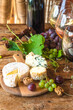 French food and drink concept; Various cheeses, nuts, grapes and glasses of wine on a wooden table;