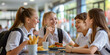 © MNStudio - Group of cheerful teenage kids sitting at the table in school cafeteria. Young students having food during lunch break in dining hall.