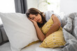 Tired sad exhausted young woman resting with closed eyes lying in bed while hugging pillow.