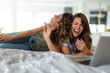 Two female friends laughing while watching funny movie scene. Two young woman enjoying their time at home, laughing hard while watching comedy film.