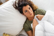 Young concerned woman feeling sick while lying in bed wrapped up in a blanket.