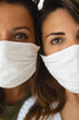 Closeup of two young women face to face looking at camera with protective face mask during quarantine due to covid-19.