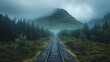   A train track snakes through a dense forest during a foggy morning with a towering mountain looming in the distance