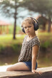 Cute little girl in modern wireless headphones enjoys music outdoors