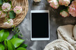 Top view to digital tablet with blank screen mockup, cozy white knitted blanket and flowers on neutral gray background