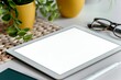 Digital tablet with blank screen mockup on table with eye glasses, notebook, potted plant. Cozy home office, small family business, entrepreneur workplace