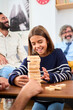 Vertical. Happy diverse generation family gathered playing Jenga at home. Caucasian people together making domestic life board games. One concentrated smiling girl is taking wooden block out of tower