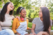 Group of young multicultural female laughing and enjoying together in park on sunny summer day. Three pretty women meeting smile excited while chatting having fun outdoors. Friendship in generation z